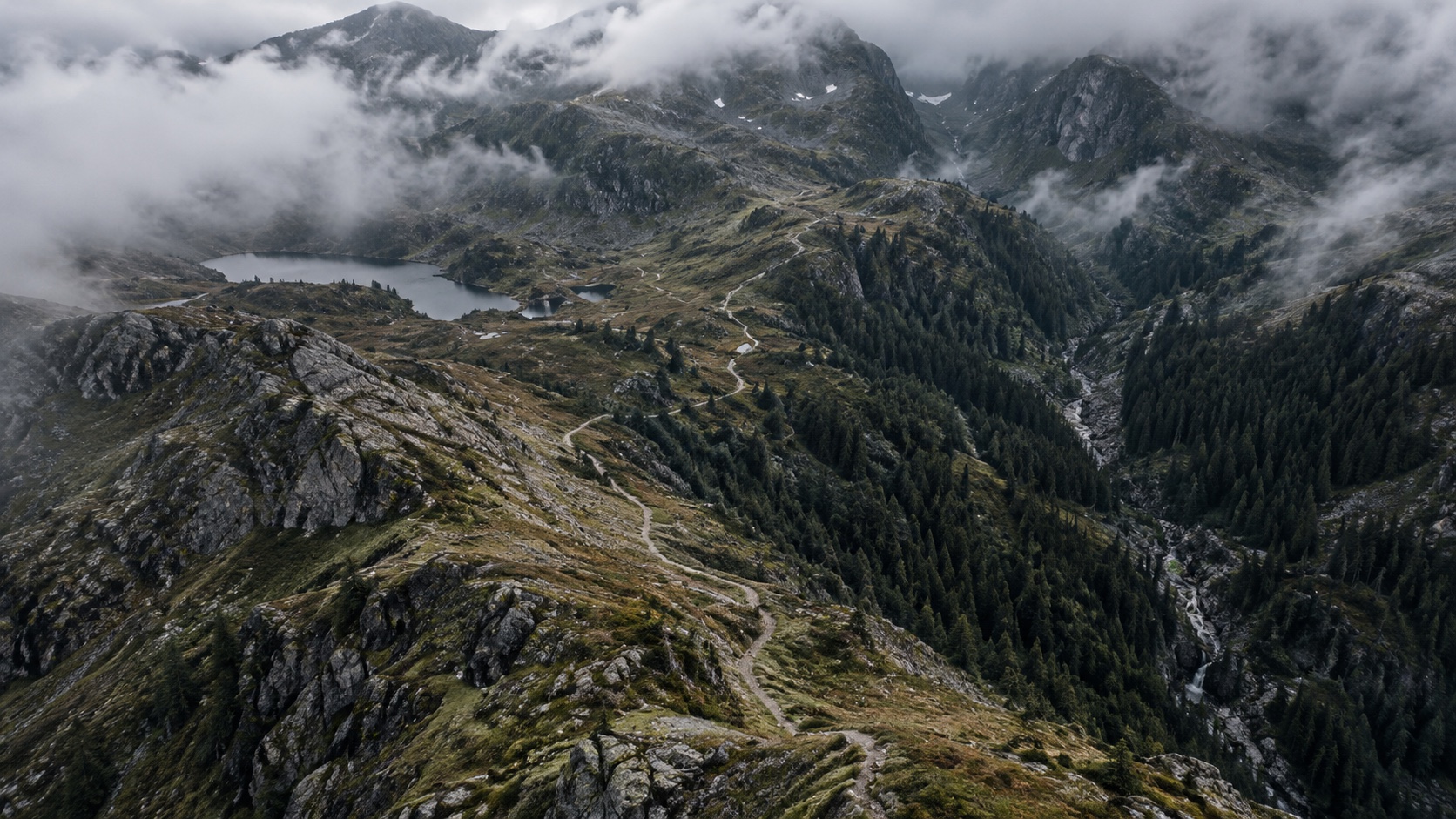 An aerial view of a mountain valley with a trail, woodland and changing elevations
